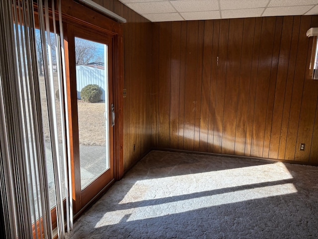 interior space featuring a healthy amount of sunlight, wood walls, a drop ceiling, and carpet flooring