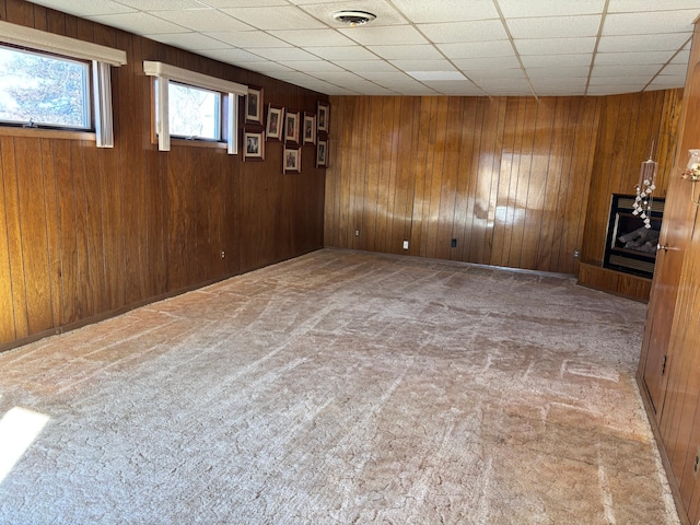 unfurnished room with carpet floors, wooden walls, visible vents, and a paneled ceiling