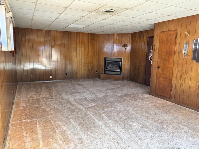 empty room with wooden walls, visible vents, a fireplace with raised hearth, carpet flooring, and a paneled ceiling