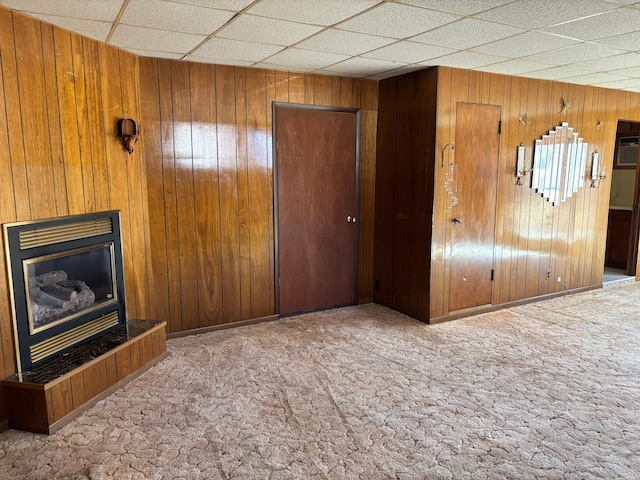 unfurnished living room with carpet floors, wood walls, a tile fireplace, and a paneled ceiling