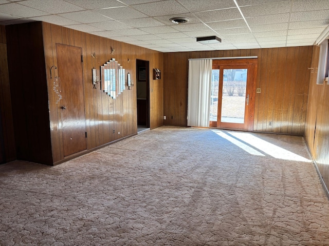 empty room featuring carpet floors, wood walls, visible vents, and a drop ceiling