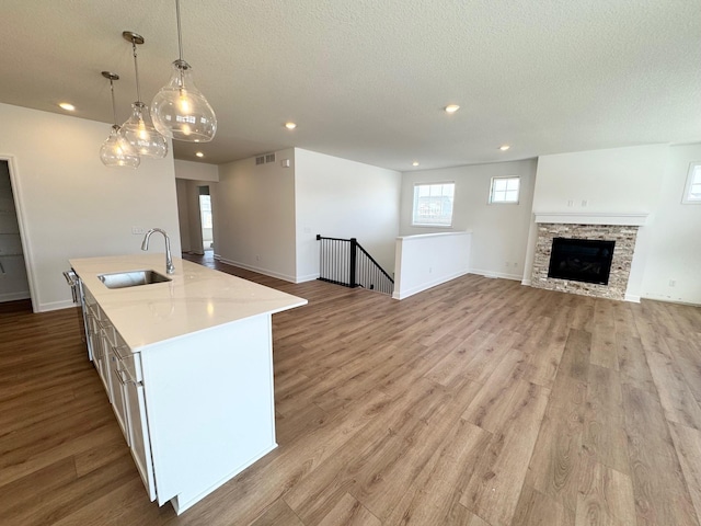 kitchen with a sink, open floor plan, hanging light fixtures, light countertops, and a center island with sink