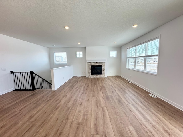 unfurnished living room featuring light wood-style flooring, a textured ceiling, visible vents, and baseboards