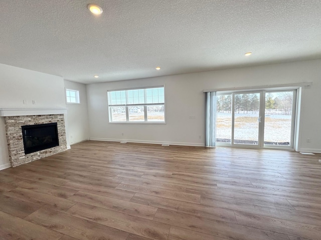 unfurnished living room with light wood-type flooring, a fireplace, plenty of natural light, and baseboards