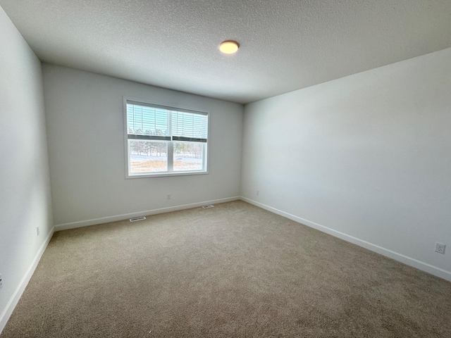 carpeted spare room featuring visible vents, baseboards, and a textured ceiling