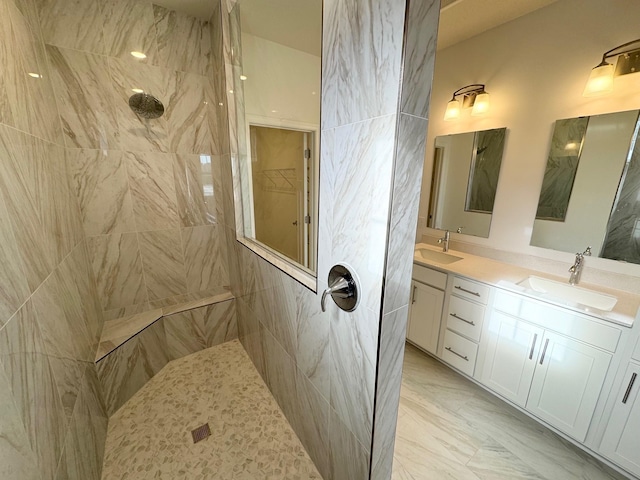 full bath featuring double vanity, marble finish floor, a sink, and tiled shower