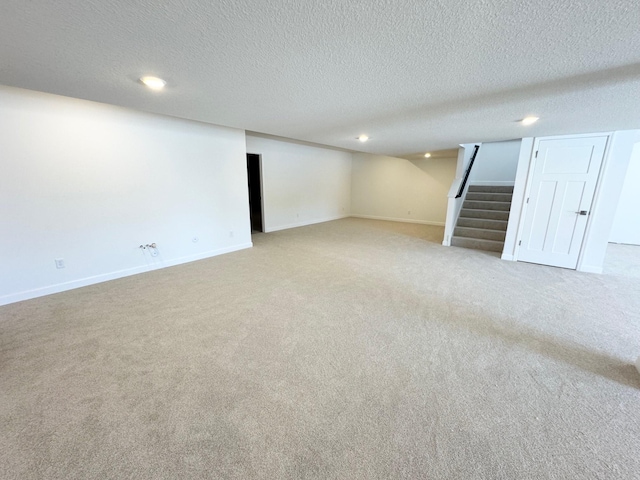 finished below grade area featuring light carpet, stairway, baseboards, and a textured ceiling