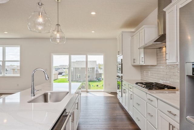 kitchen with decorative light fixtures, stainless steel appliances, white cabinetry, a sink, and wall chimney exhaust hood