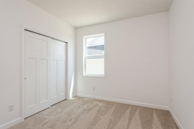 unfurnished bedroom with light carpet, a closet, visible vents, and baseboards