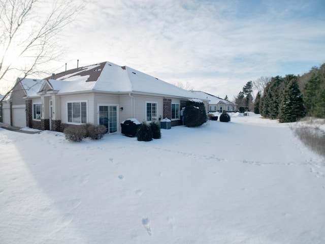 snow covered property with a garage and brick siding