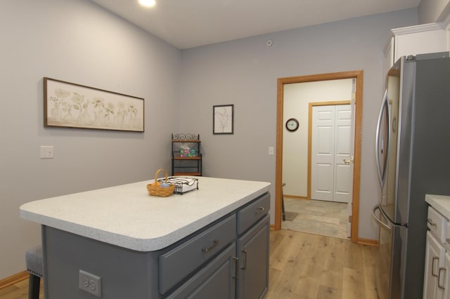 kitchen featuring white cabinets, a center island, freestanding refrigerator, light countertops, and gray cabinetry