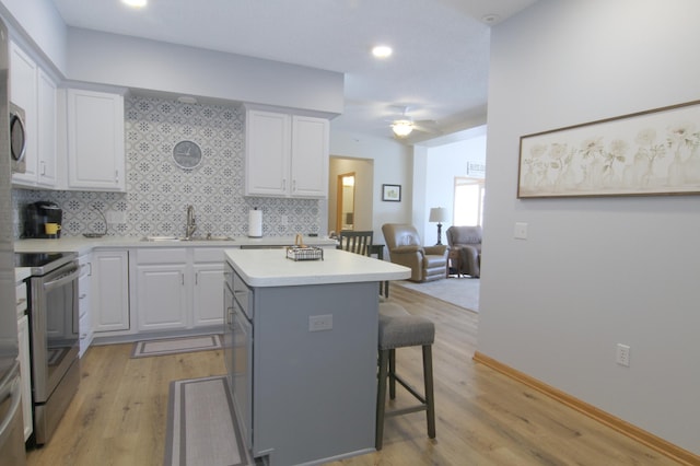 kitchen with a breakfast bar, a center island, stainless steel electric range oven, open floor plan, and white cabinetry