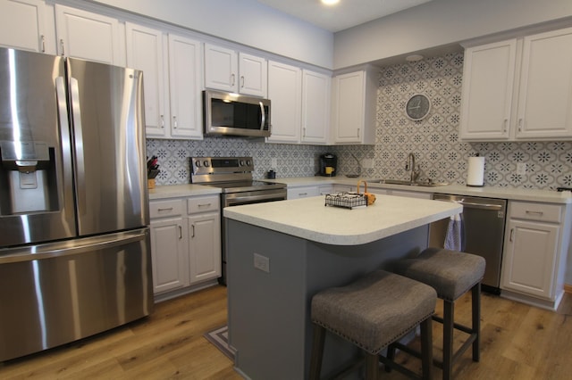 kitchen featuring a kitchen island, stainless steel appliances, light countertops, white cabinetry, and a sink