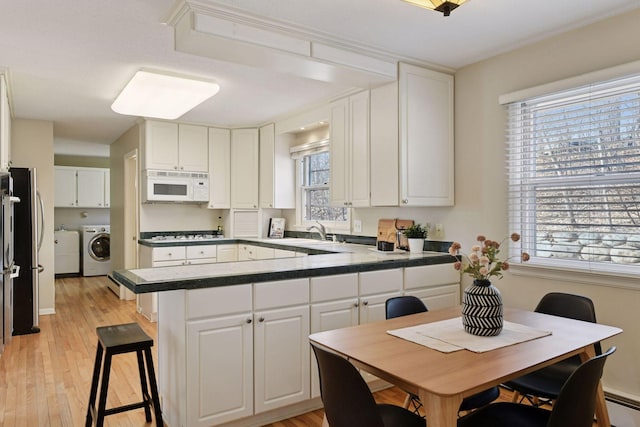 kitchen featuring white microwave, a peninsula, a sink, white cabinetry, and independent washer and dryer