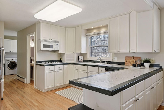 kitchen with white appliances, a peninsula, washer / clothes dryer, and white cabinets