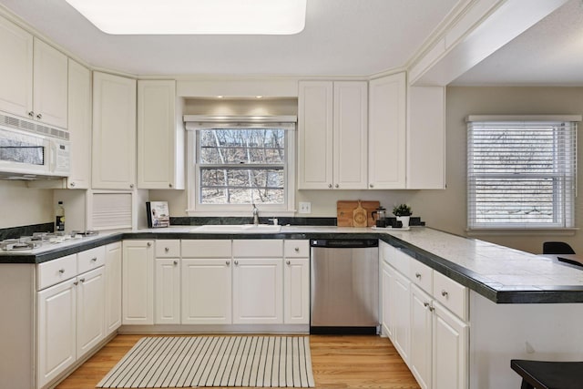 kitchen featuring white appliances, a peninsula, a sink, light wood-style floors, and white cabinetry