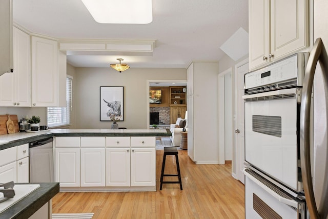 kitchen featuring a brick fireplace, light wood-type flooring, a peninsula, stainless steel appliances, and white cabinetry