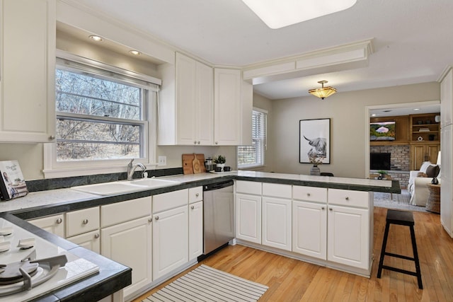 kitchen with a peninsula, a fireplace, a sink, stainless steel dishwasher, and light wood-type flooring