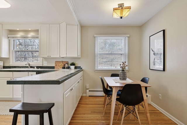 kitchen featuring light wood-style flooring, dark countertops, white cabinetry, a peninsula, and baseboard heating