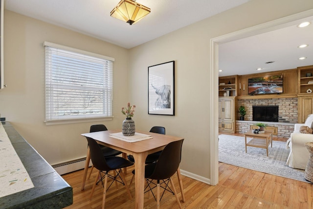 dining area with light wood-type flooring, a baseboard heating unit, baseboards, and a fireplace