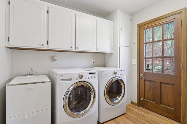 washroom featuring washing machine and dryer, cabinet space, and light wood-style flooring