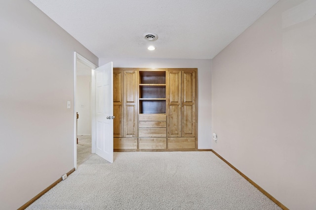 unfurnished bedroom featuring light carpet, visible vents, a textured ceiling, and baseboards