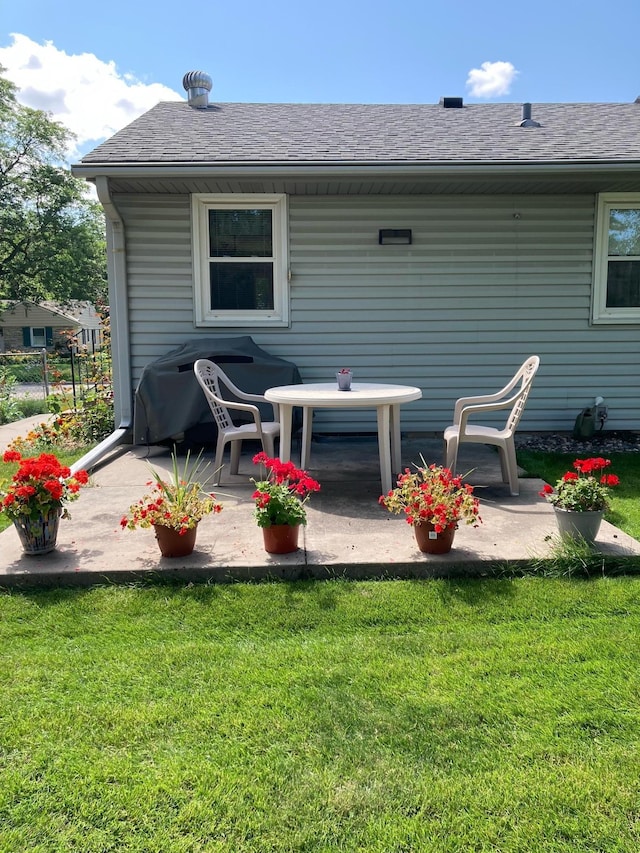 back of property with a yard, a shingled roof, and a patio area