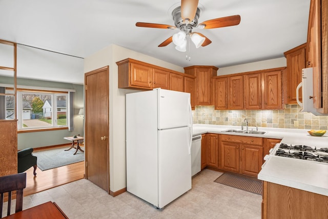 kitchen with white appliances, tasteful backsplash, brown cabinetry, and a sink