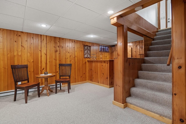 sitting room with baseboard heating, stairway, carpet, and wood walls