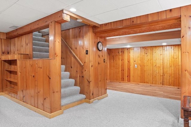 finished basement featuring carpet floors, wooden walls, stairs, and baseboards