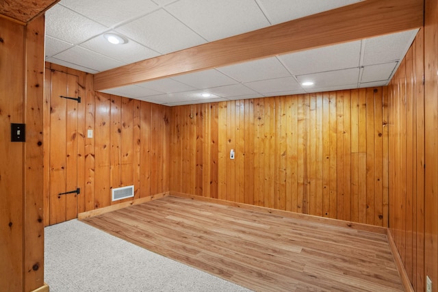 unfurnished room featuring visible vents, wood walls, wood finished floors, a drop ceiling, and baseboards