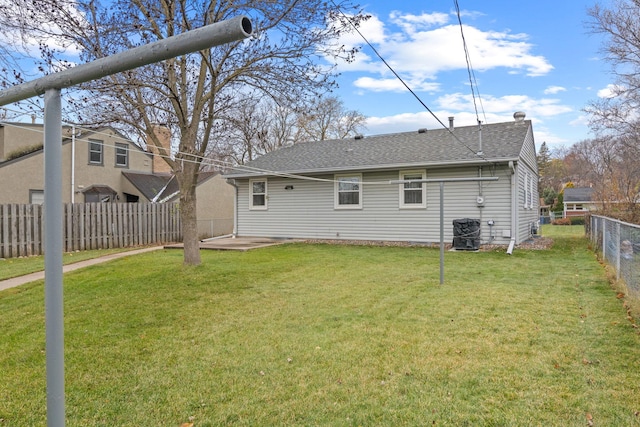 rear view of house with a fenced backyard, a lawn, and roof with shingles