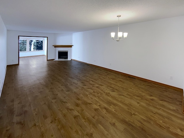 unfurnished living room featuring dark wood-type flooring, a chandelier, a fireplace, and baseboards