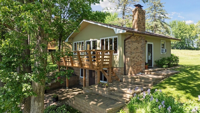 rear view of property with brick siding, a chimney, a deck, and a yard