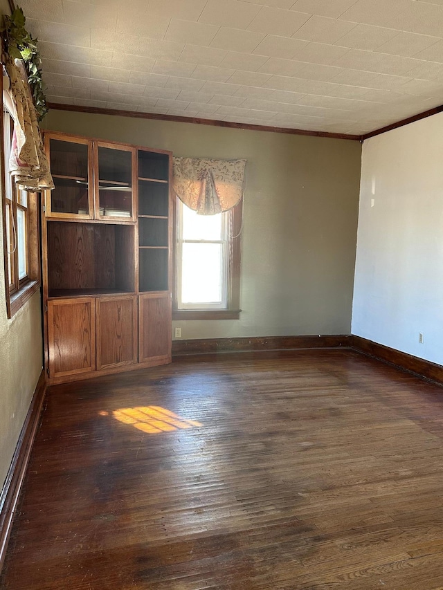 empty room with baseboards, ornamental molding, and dark wood-type flooring