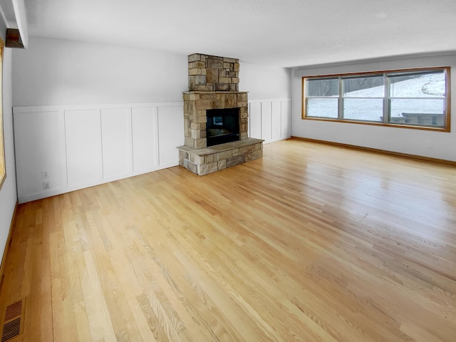 unfurnished living room featuring a wainscoted wall, a fireplace, visible vents, a decorative wall, and wood finished floors