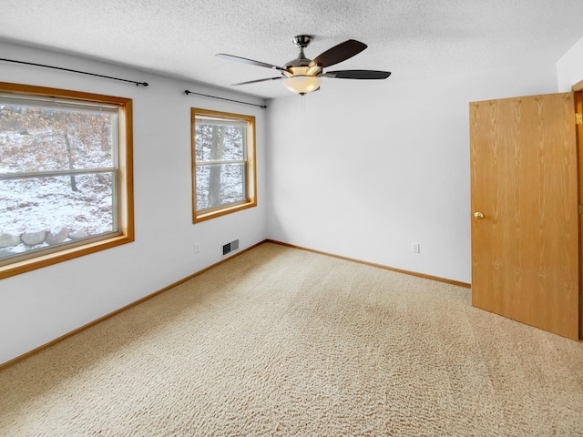 carpeted empty room featuring a ceiling fan, visible vents, a textured ceiling, and baseboards