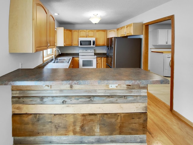 kitchen featuring dark countertops, a sink, a textured ceiling, white appliances, and a peninsula