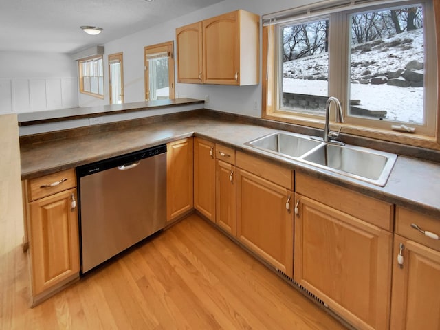 kitchen with dark countertops, a sink, light wood finished floors, and stainless steel dishwasher