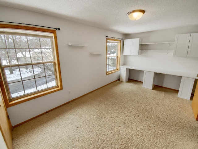 unfurnished office featuring a textured ceiling, light colored carpet, and baseboards