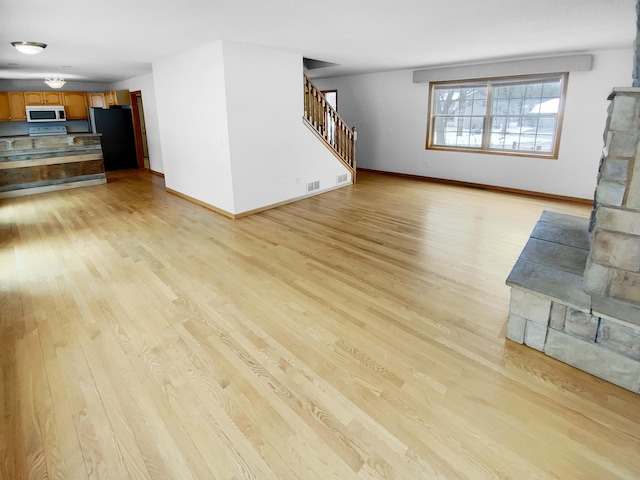 unfurnished living room with light wood-style floors, visible vents, baseboards, and stairs