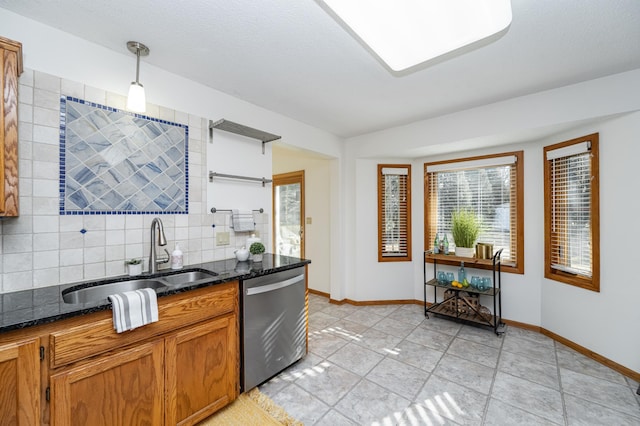 kitchen with dark stone countertops, brown cabinetry, a sink, dishwasher, and tasteful backsplash