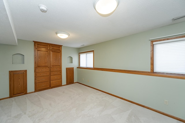 unfurnished bedroom featuring a textured ceiling, baseboards, visible vents, and light carpet