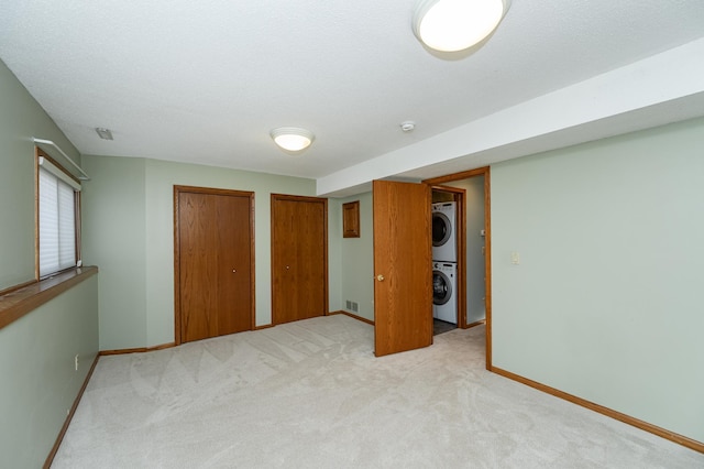 unfurnished bedroom with two closets, a textured ceiling, stacked washer / drying machine, baseboards, and light colored carpet