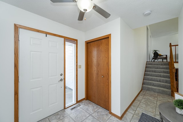 foyer featuring stairway, a ceiling fan, baseboards, visible vents, and a textured ceiling