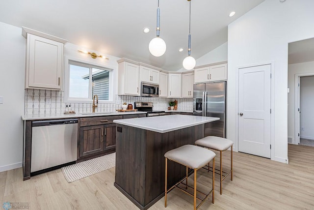 kitchen with decorative backsplash, stainless steel appliances, a kitchen bar, white cabinetry, and a sink