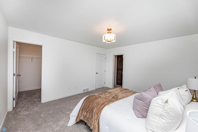 bedroom with a spacious closet, carpet flooring, visible vents, and baseboards