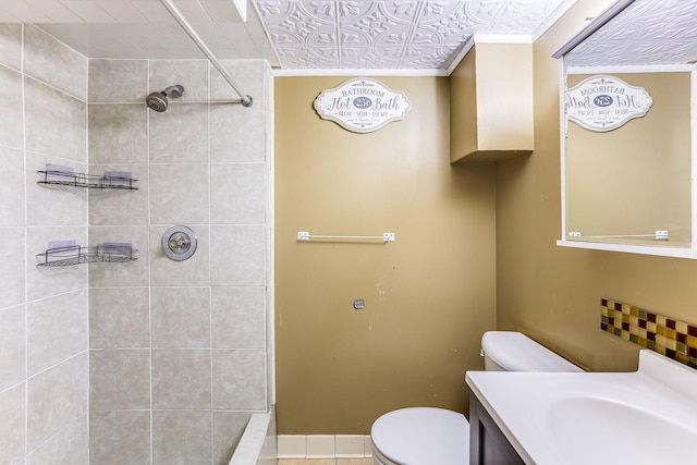 bathroom featuring vanity, a tile shower, toilet, and crown molding