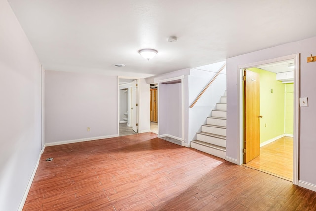 spare room featuring light wood-style floors, stairway, and baseboards