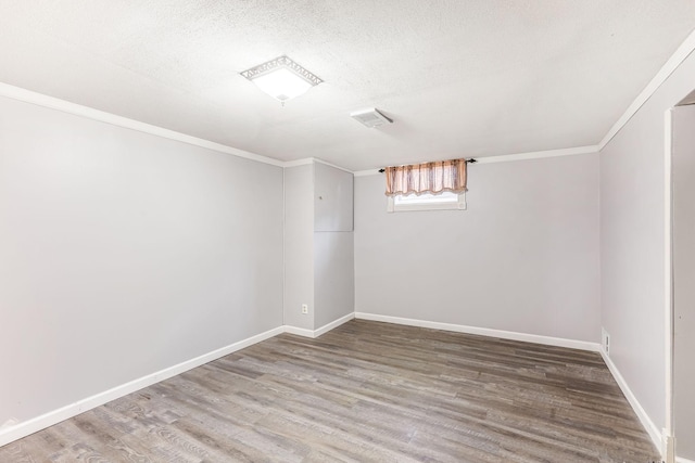 empty room with baseboards, visible vents, wood finished floors, crown molding, and a textured ceiling